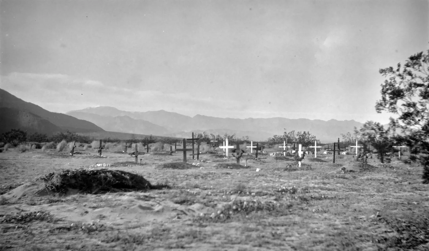 Black and white photograph of a graveyard with black and white crosses with hills in the distance.