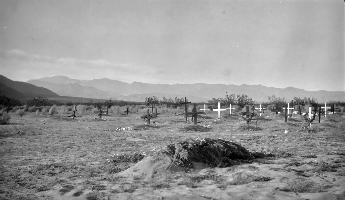 Black and white photograph of a graveyard with black and white wooden crosses and hills in the distance.