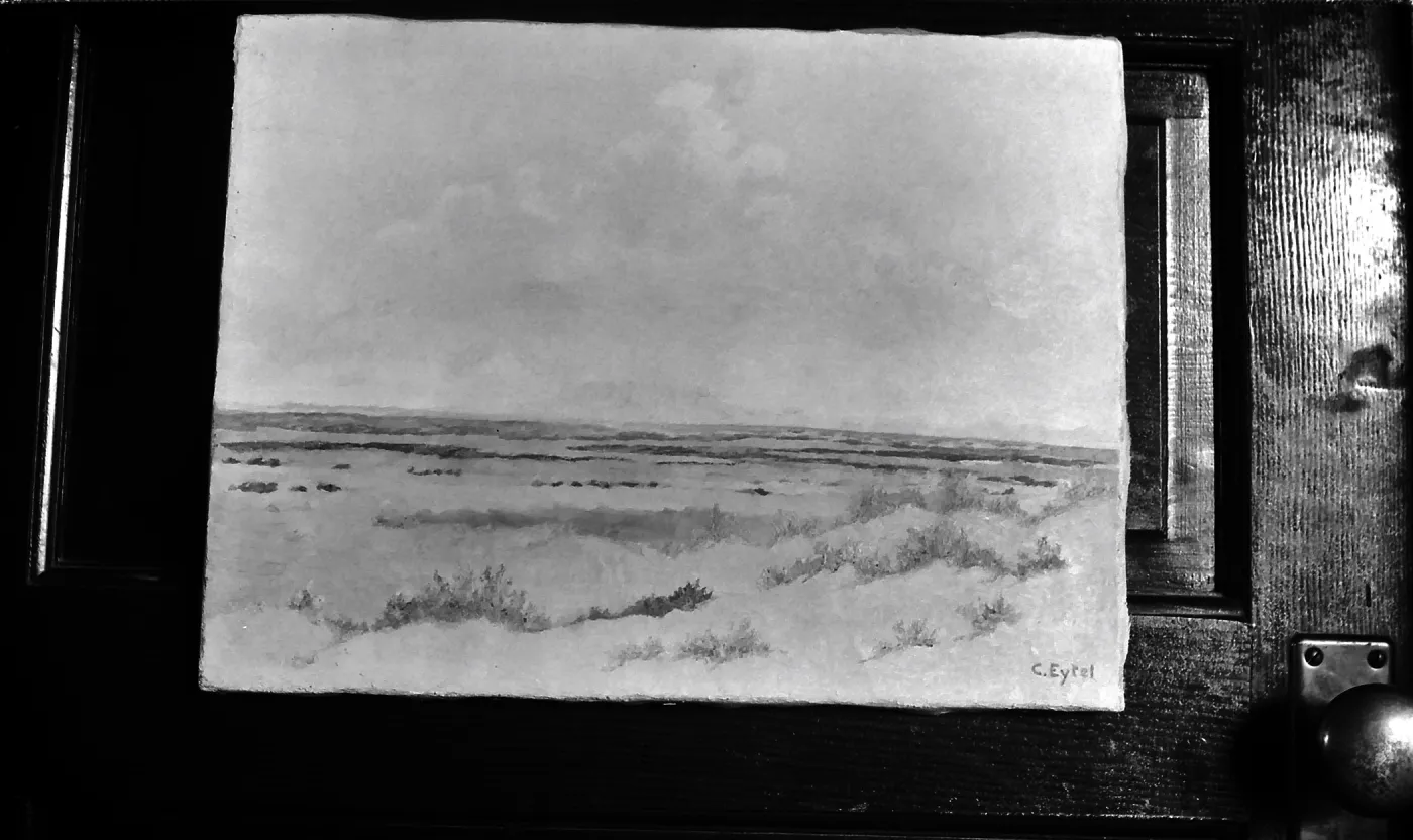 Black and white photograph of a painting of a desert landscape with the signature C Eytel taken against a door.