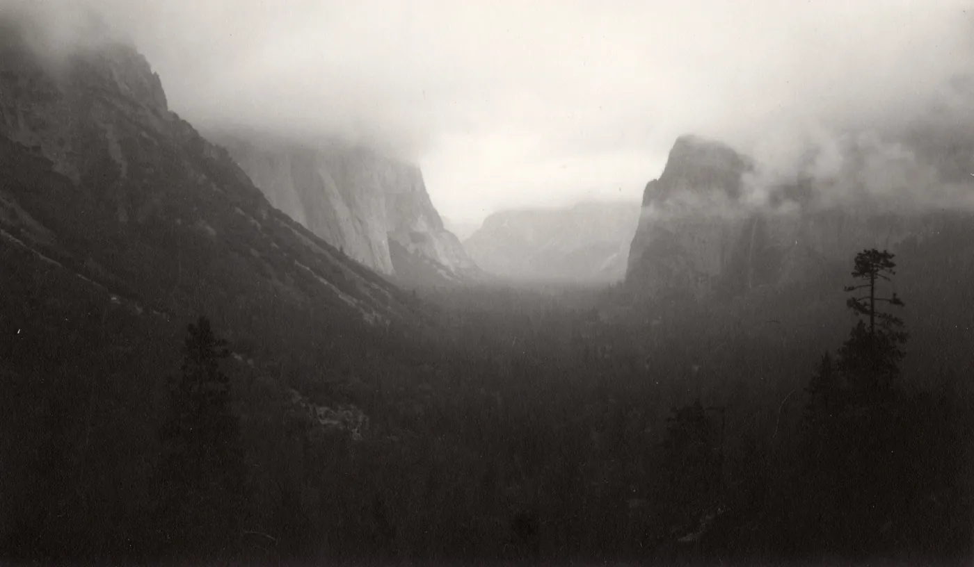 Black and white photograph of mountain range with fog covering mountain tops.