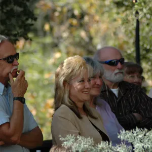 A group of people in a tree grove, all looking off camera at something. Two men and two women are in focus. The two men have their arms are crossed and the two women are smiling.