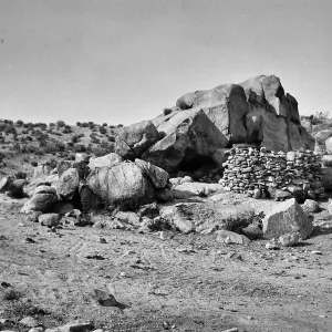 Black and white photograph of a manmade rock formation on top of a large flat rock.