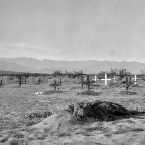 Black and white photograph of a graveyard with black and white wooden crosses and hills in the distance.