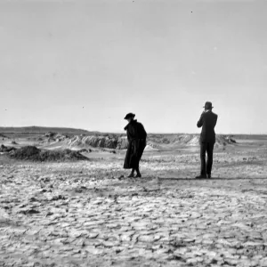 Black and white photograph of a man and woman standing on a dried-up mud flat that extends far into the distance.