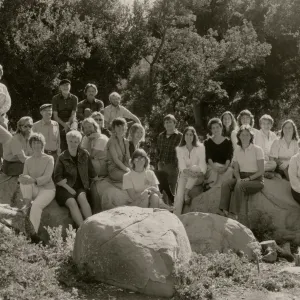 A black and white photo of 27 people are posed sitting atop or standing around several boulders a the edge of a forest.