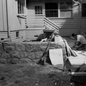 Patio & stone walls under construction in the Home Demonstration Garden. Workman laying flagstone