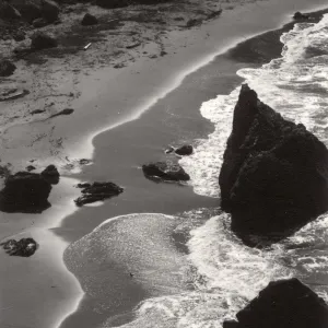 Black and white photograph of coast line with large rocks in waves.