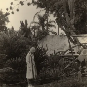 Black and white photograph of woman standing in garden bed looking down at plants.
