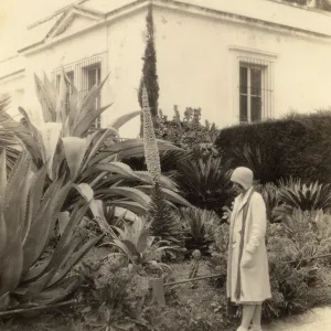 Black and white photograph of woman looking a plant bed in front of white building.